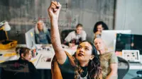 Businesswoman explaining strategy to colleagues while writing on glass at IT company