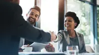 Happy couple at a table completing paperwork. Woman is shaking hands with the bank representative.